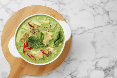 Photo of Saucepan with delicious green curry chicken soup on white marble table, top view. Space for text
