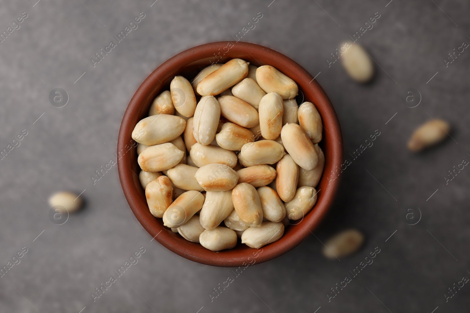 Photo of Roasted peanuts in bowl on brown table, top view