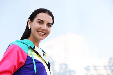 Young sportswoman with wireless earphones on city street