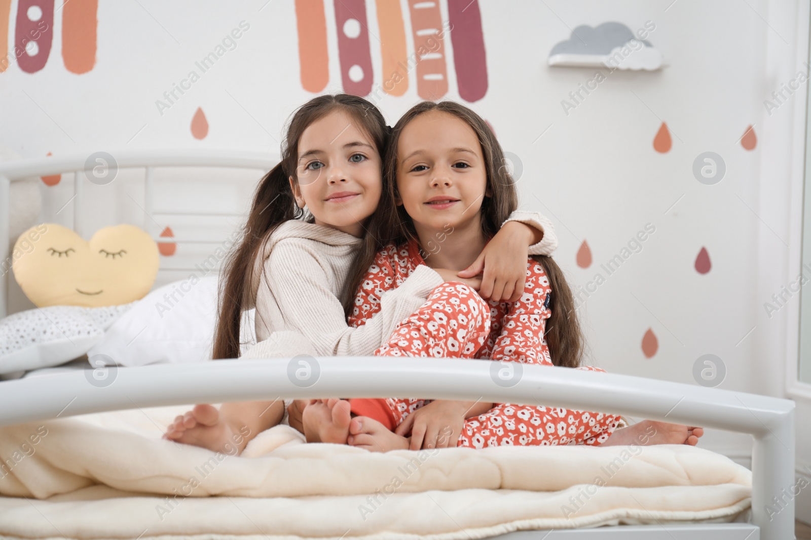 Photo of Cute girls in pajamas on bed at home