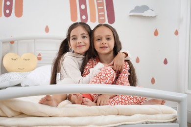 Photo of Cute girls in pajamas on bed at home