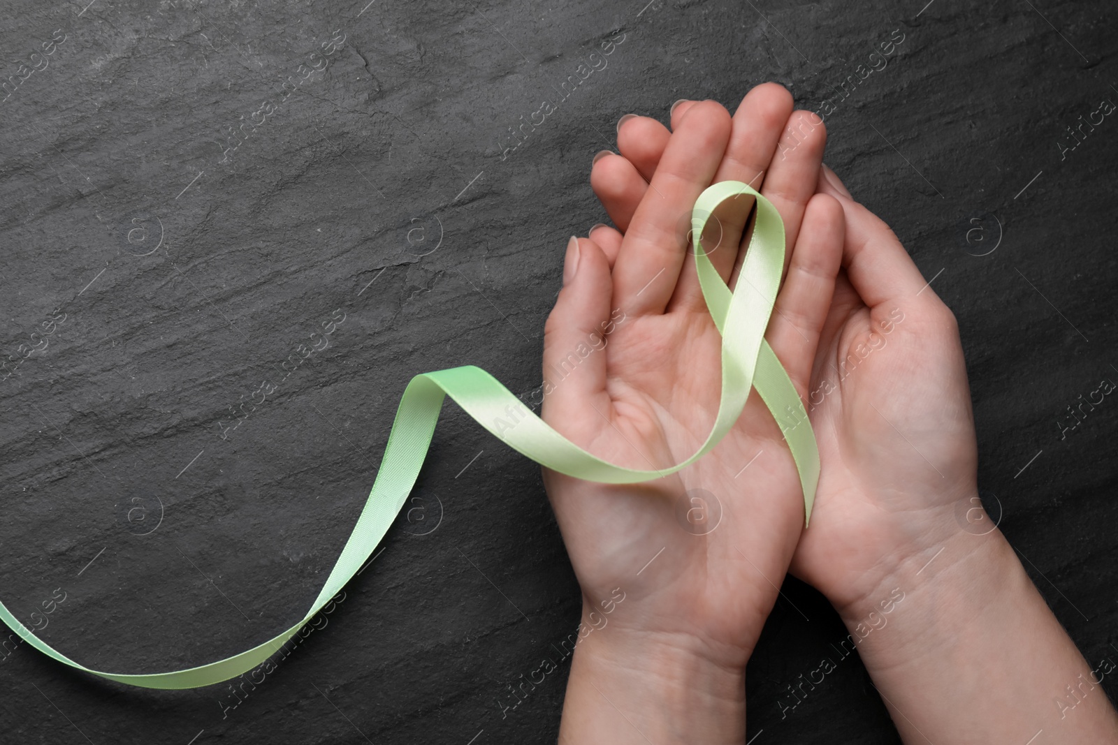 Photo of World Mental Health Day. Woman holding green ribbon on black background, top view with space for text