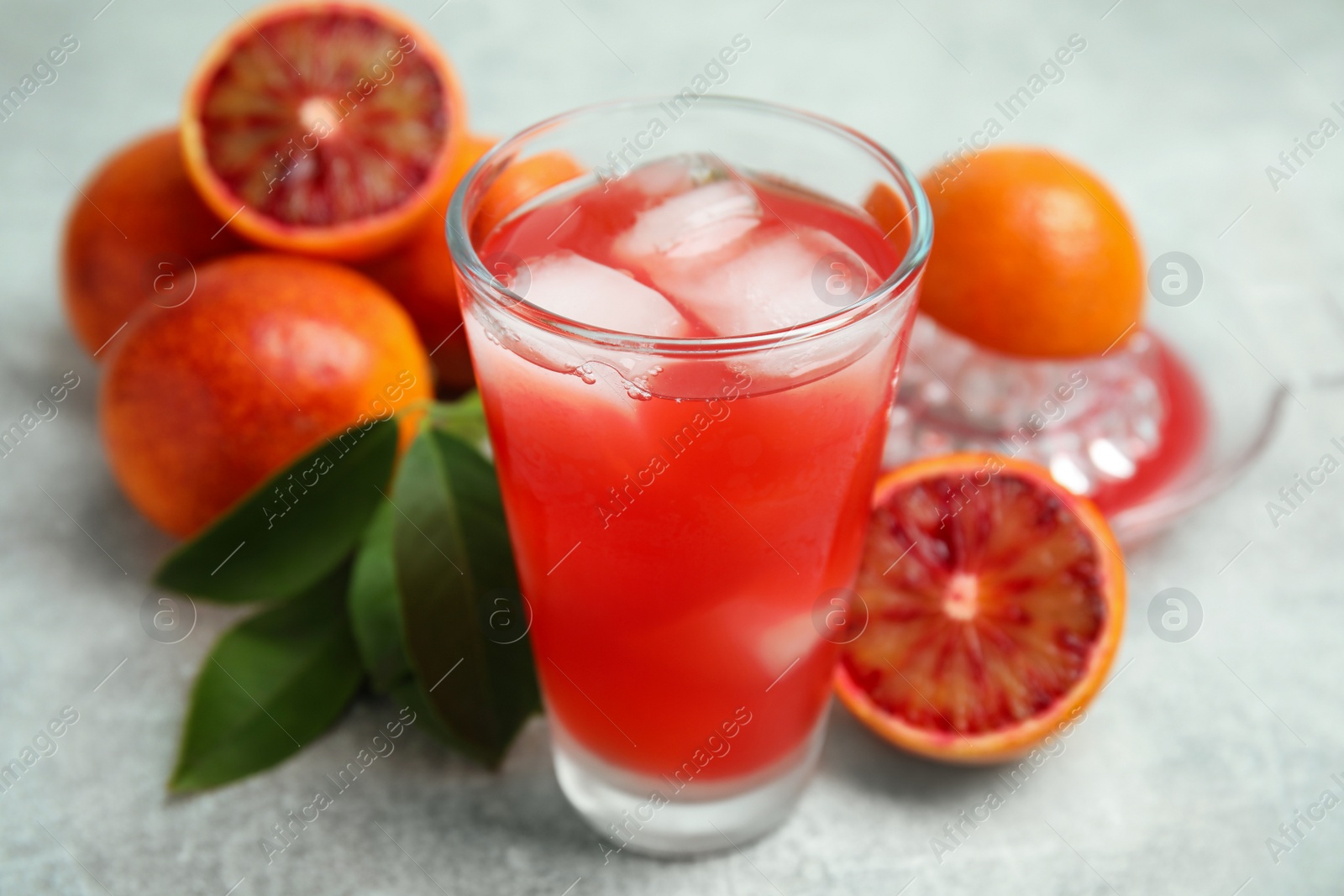 Photo of Tasty sicilian orange juice with ice cubes in glass and fruits on light grey table, closeup