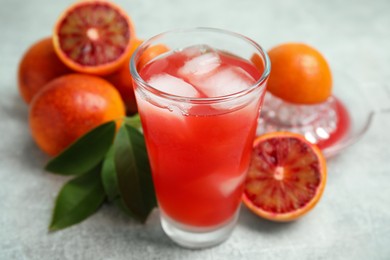 Photo of Tasty sicilian orange juice with ice cubes in glass and fruits on light grey table, closeup