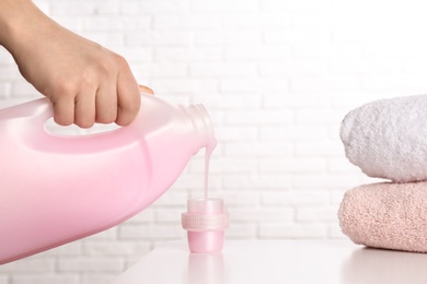 Woman pouring detergent into cap on table against brick wall, closeup. Laundry day