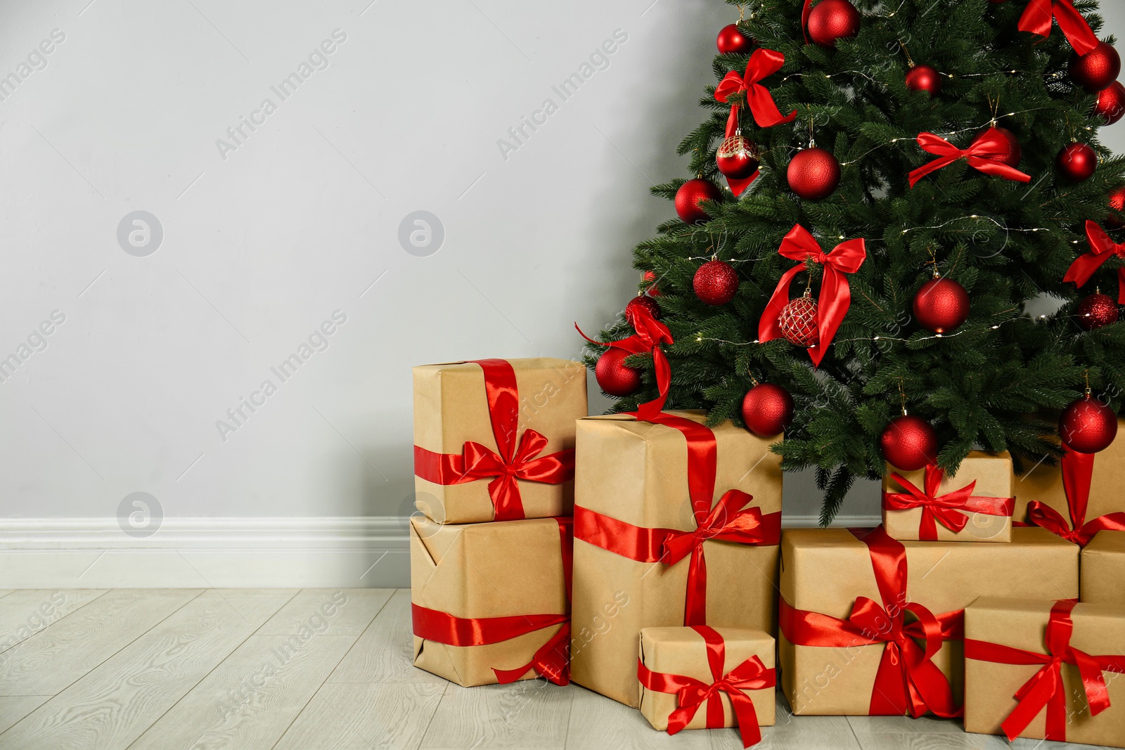 Photo of Decorated Christmas tree and gift boxes near light wall. Space for text