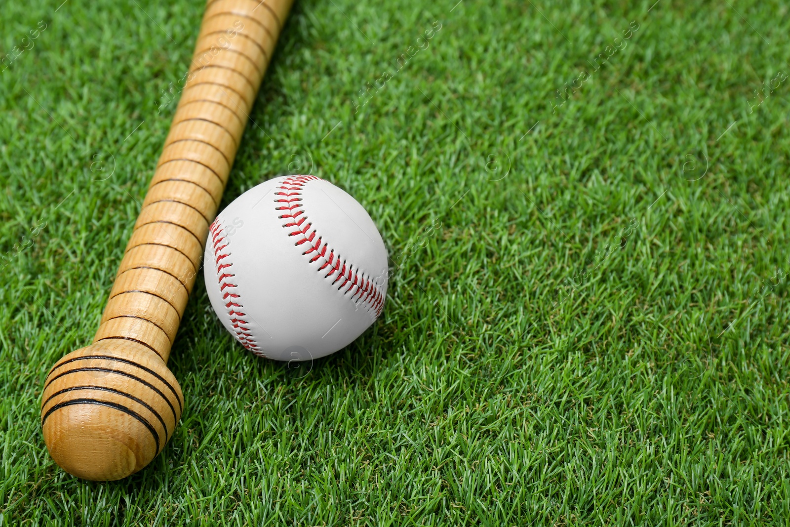 Photo of Wooden baseball bat and ball on green grass, closeup. Space for text