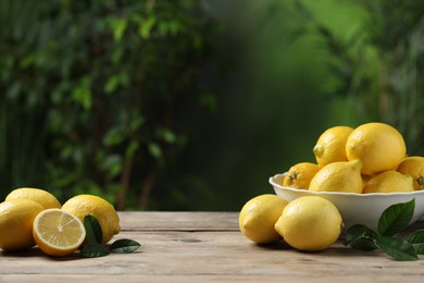 Fresh lemons and green leaves on wooden table. Space for text