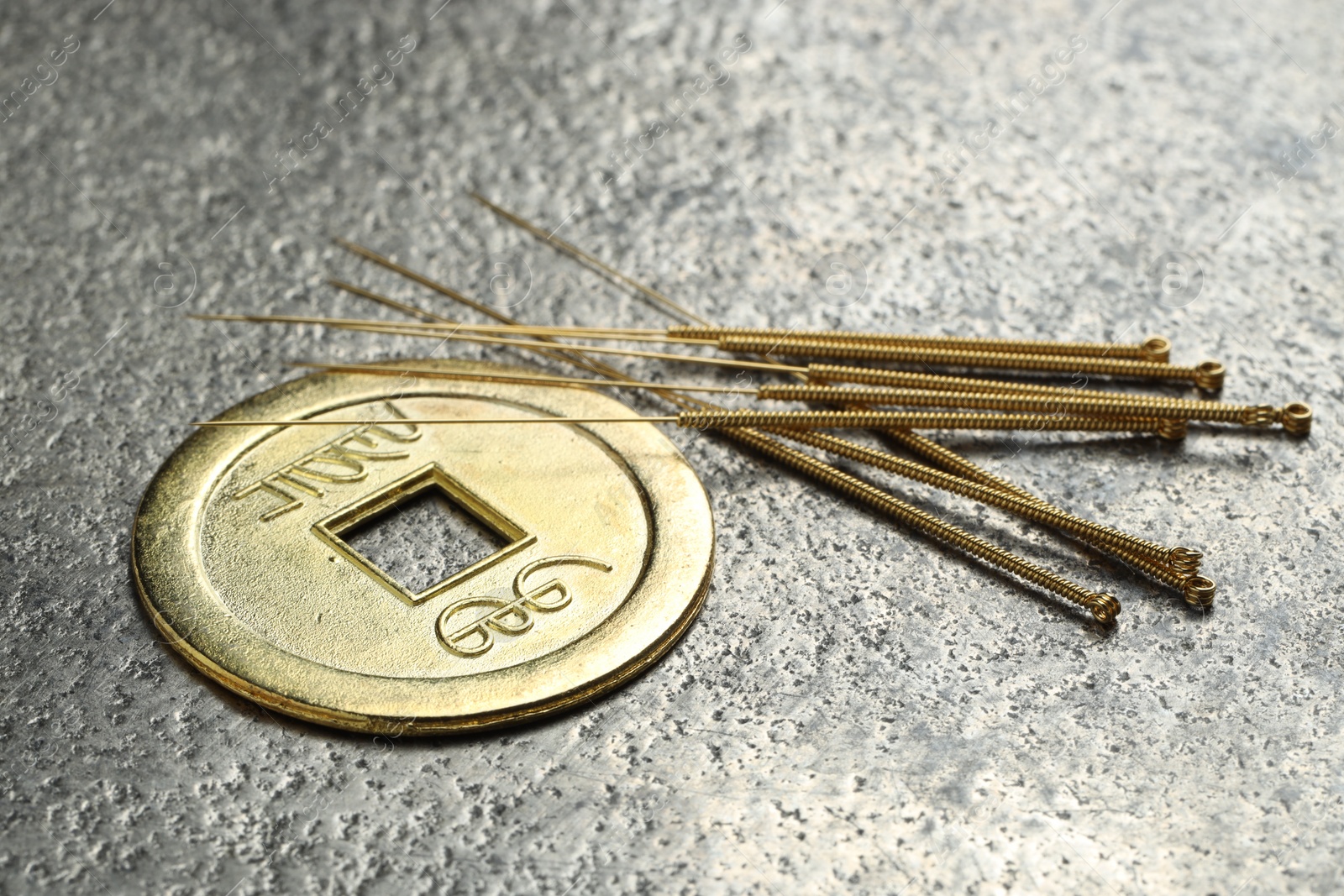 Photo of Acupuncture needles and Chinese coin on grey textured table, closeup