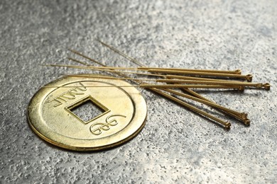 Photo of Acupuncture needles and Chinese coin on grey textured table, closeup
