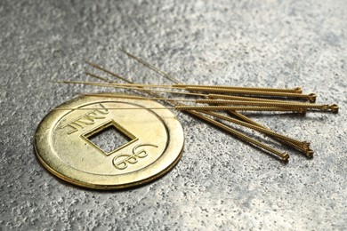 Acupuncture needles and Chinese coin on grey textured table, closeup