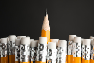 Photo of One pencil with sharp point standing out from others on black background, closeup