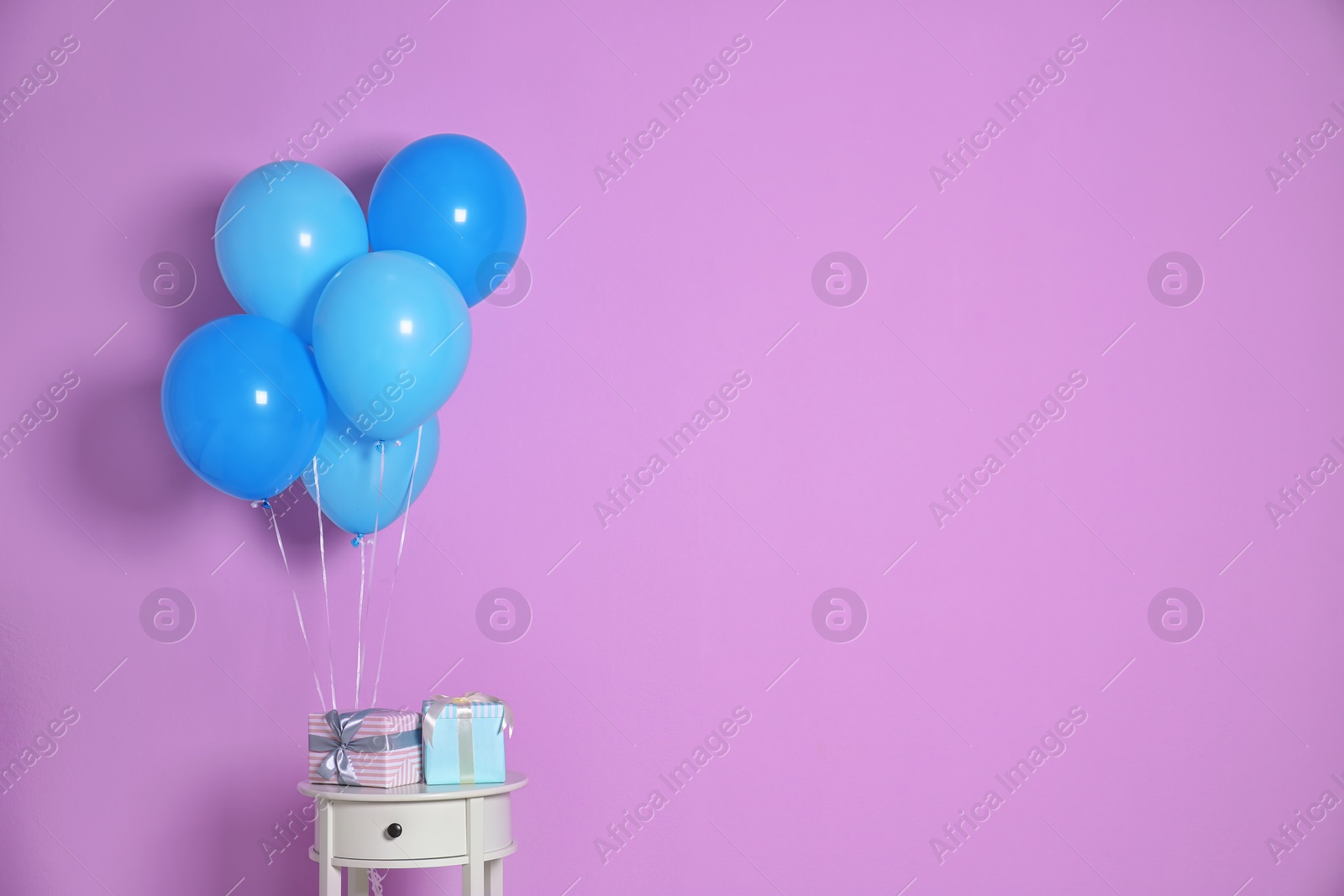 Photo of Bunch of bright balloons and gifts on table against color wall. Space for text