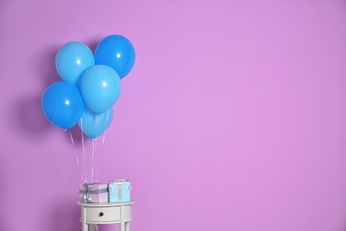 Photo of Bunch of bright balloons and gifts on table against color wall. Space for text