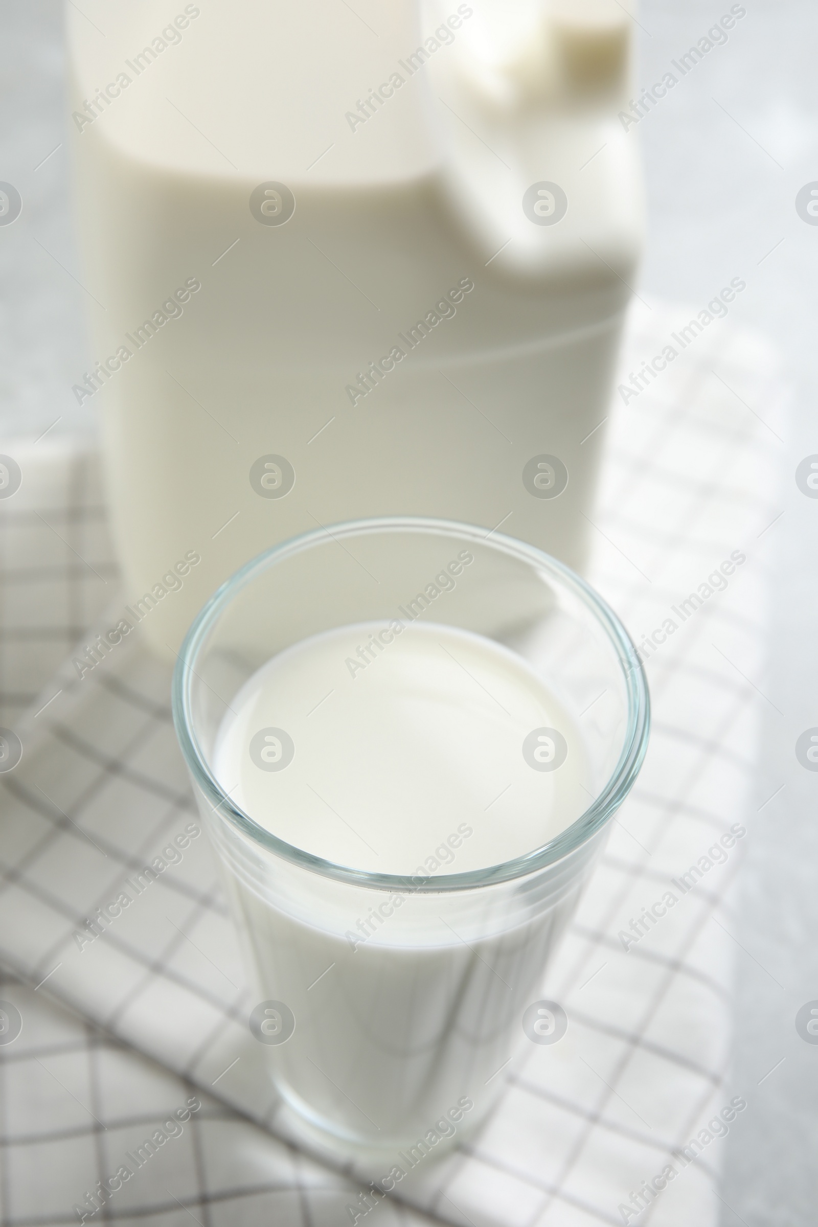 Photo of Glass of milk near gallon bottle on light table, closeup