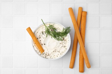 Photo of Delicious cream cheese with grissini sticks and dill on white tiled table, flat lay