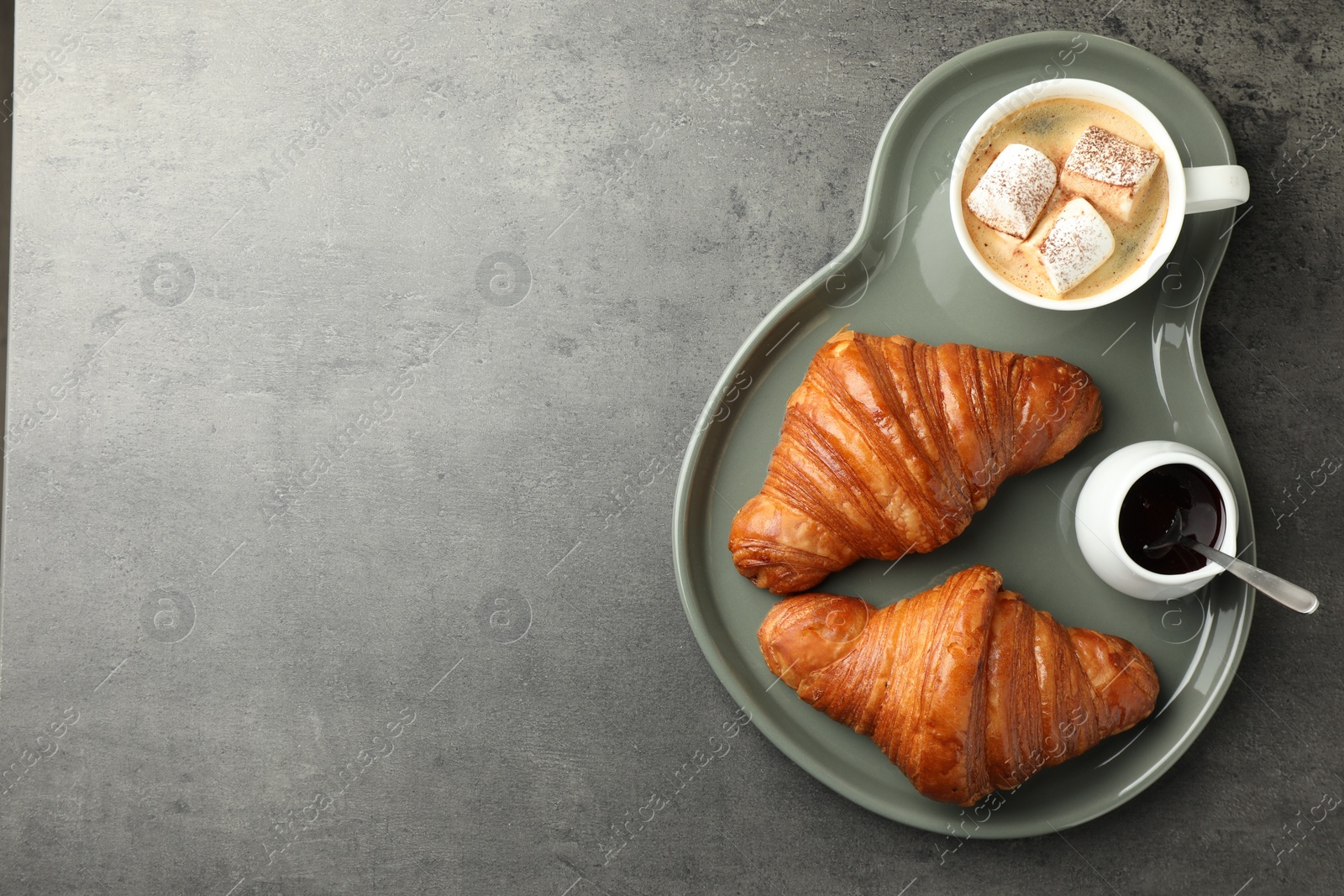 Photo of Tasty croissants served with cup of hot drink on grey textured table, top view. Space for text