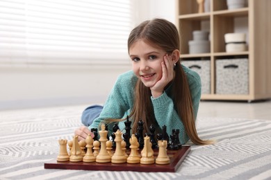 Photo of Cute girl playing chess on floor in room