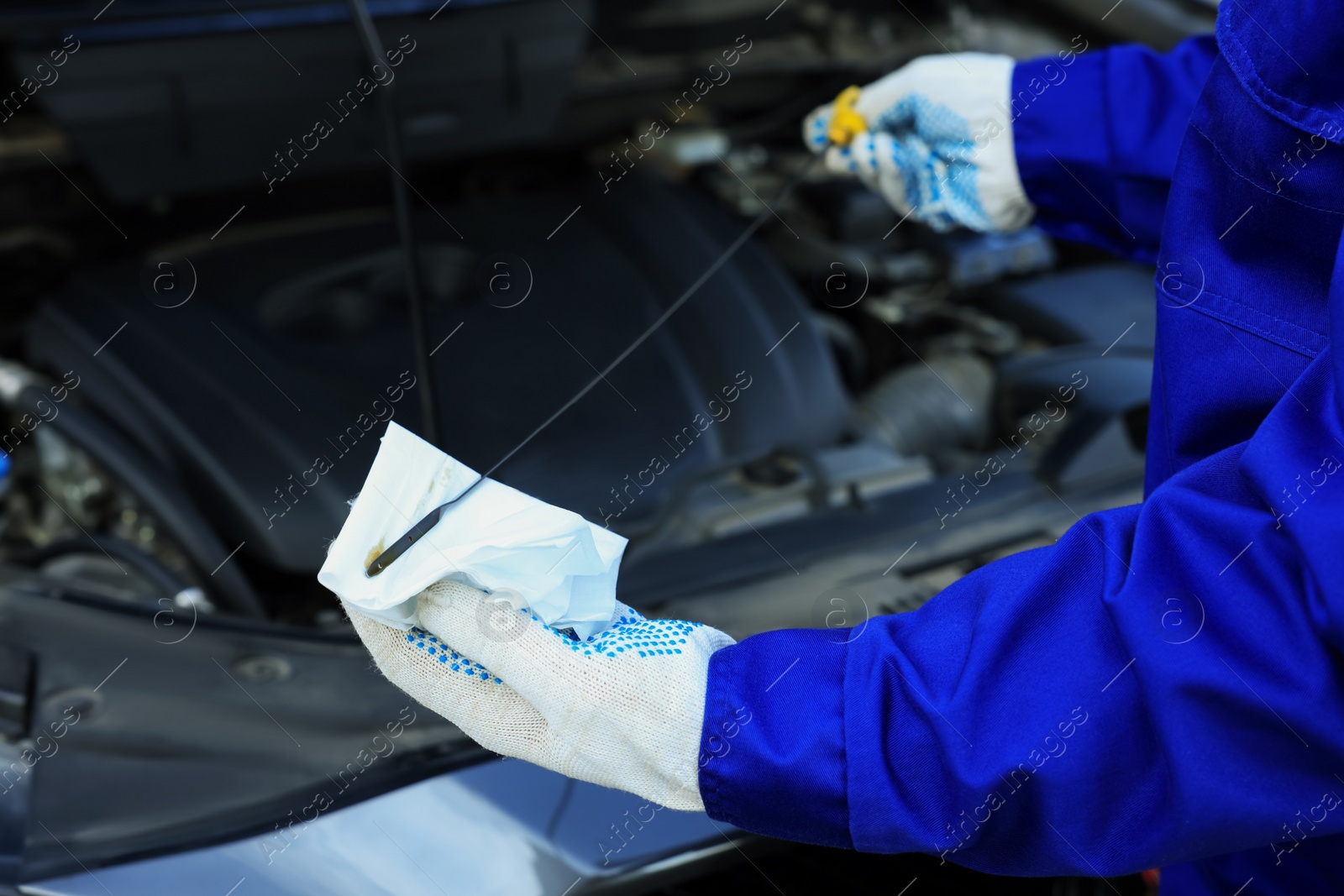 Photo of Worker checking motor oil level in car with dipstick, closeup