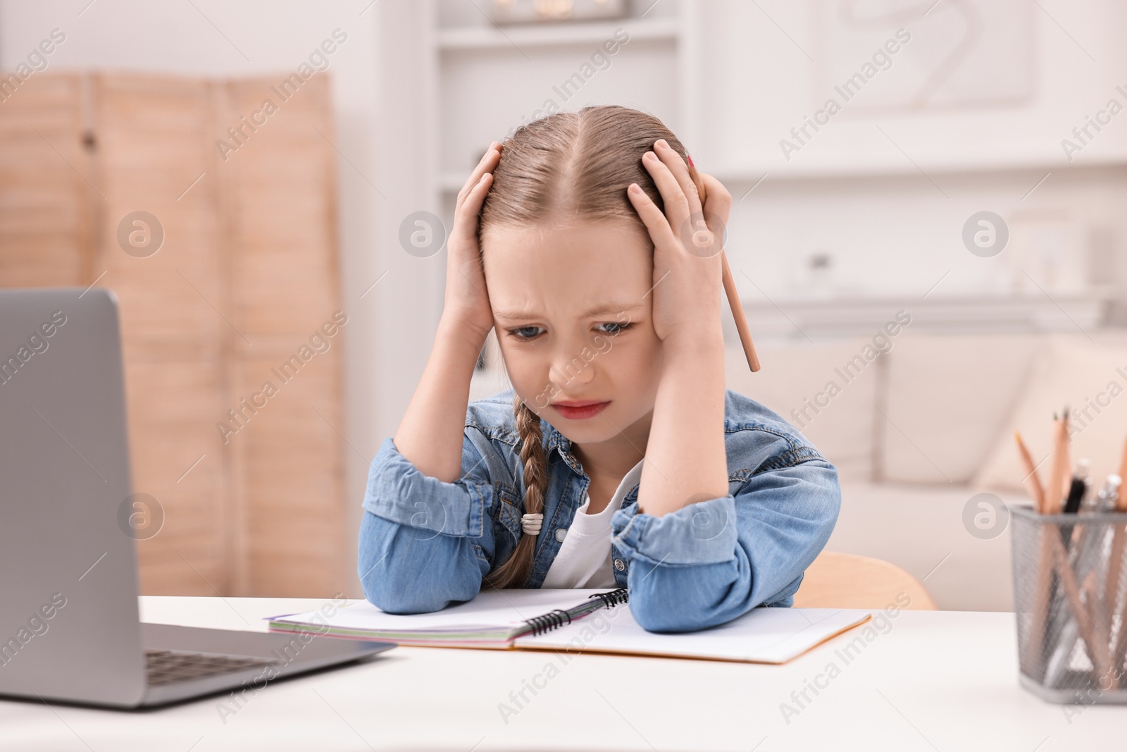 Photo of Little girl suffering from headache while doing homework at home