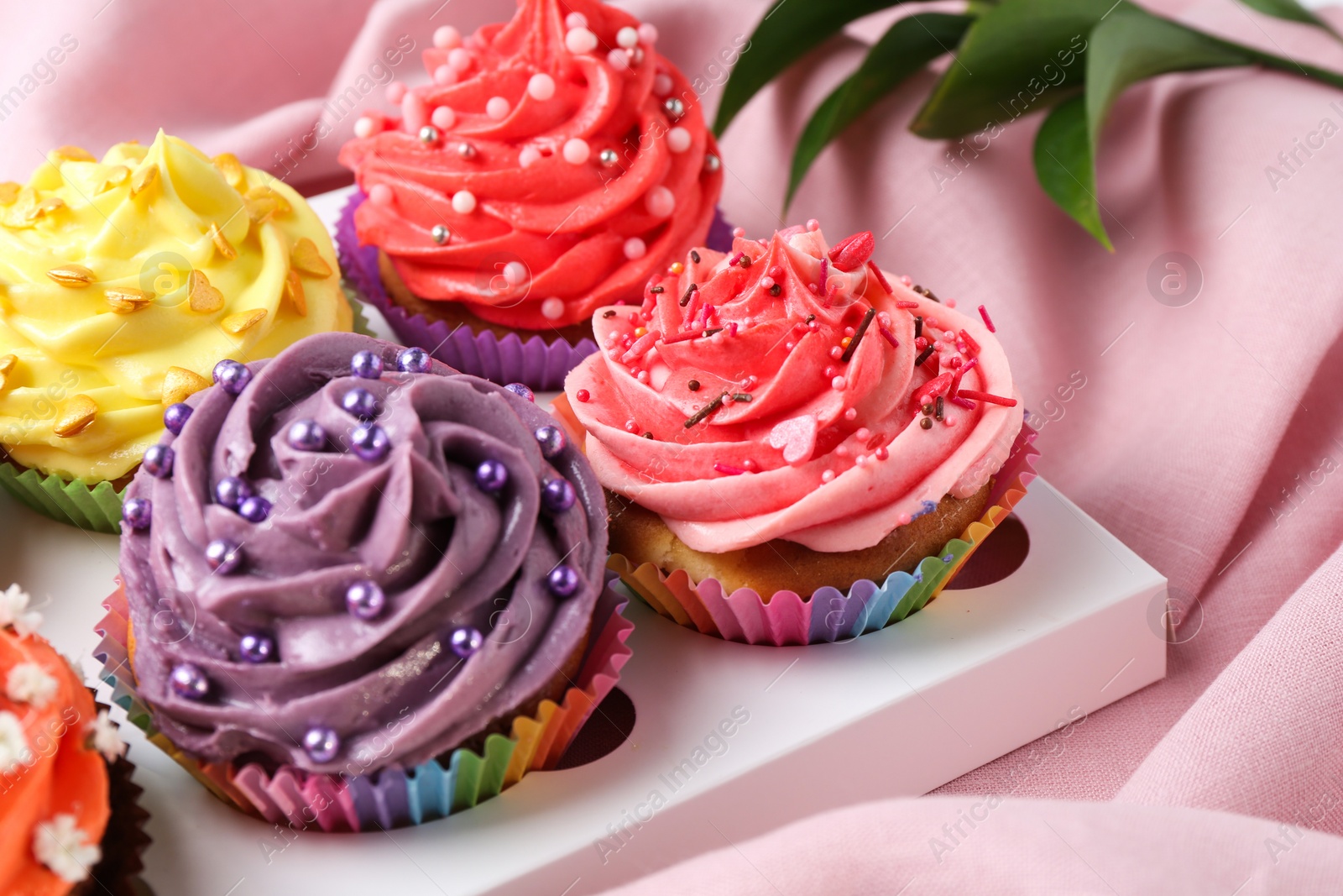 Photo of Delicious cupcake with bright cream on pink fabric, closeup