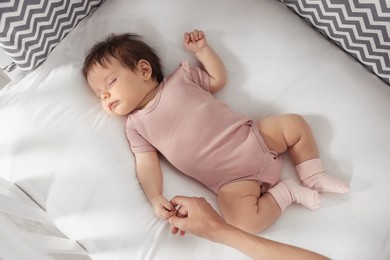 Photo of Mother holding hand of her baby on bed, top view