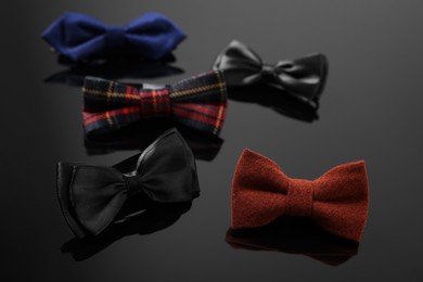 Photo of Stylish color bow ties on black mirror surface