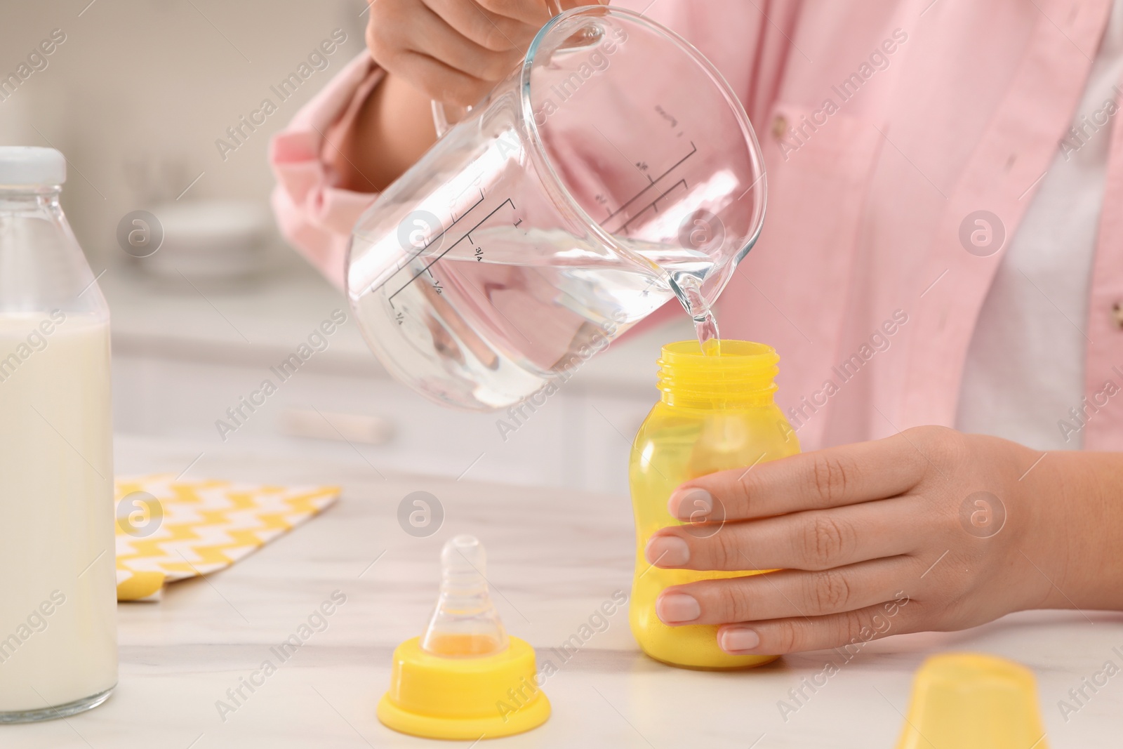 Photo of Woman preparing infant formula at table indoors, closeup. Baby milk