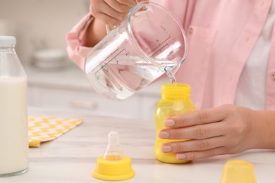 Photo of Woman preparing infant formula at table indoors, closeup. Baby milk