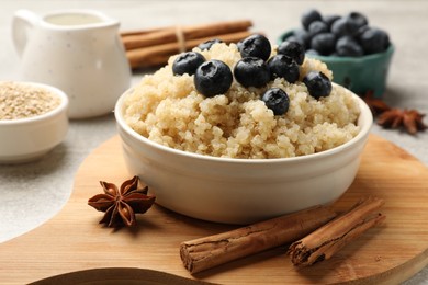 Photo of Tasty quinoa porridge with blueberries in bowl and spices on table, closeup