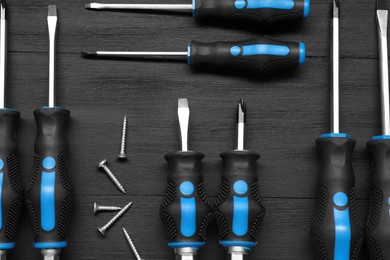 Photo of Set of screwdrivers and screws on black wooden table, flat lay