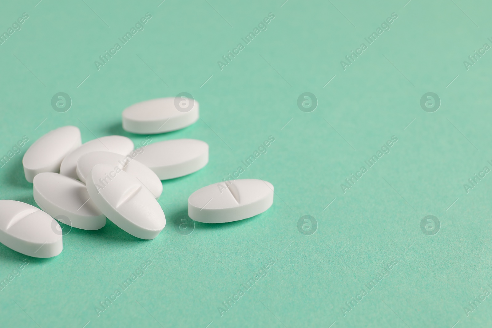 Photo of Pile of white pills on green background, closeup. Space for text