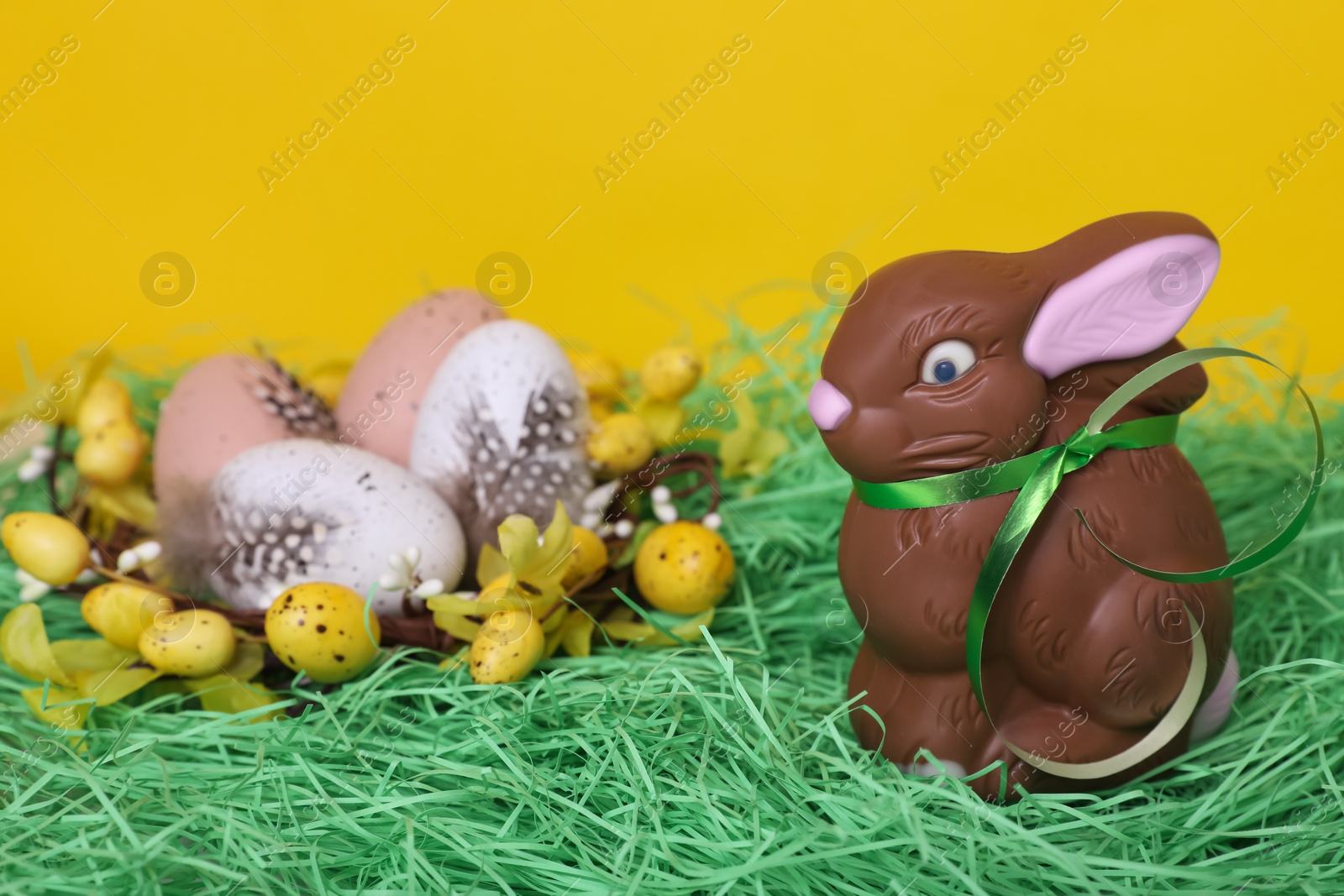 Photo of Easter celebration. Cute chocolate bunny and different eggs with feathers on grass against yellow background