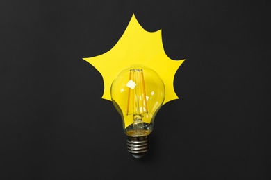 Photo of Lamp bulb with yellow paper imitating light on black background, flat lay