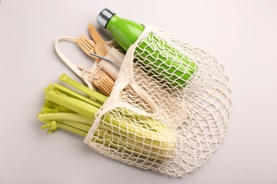 Photo of Fishnet bag with different items on light grey background, top view. Conscious consumption
