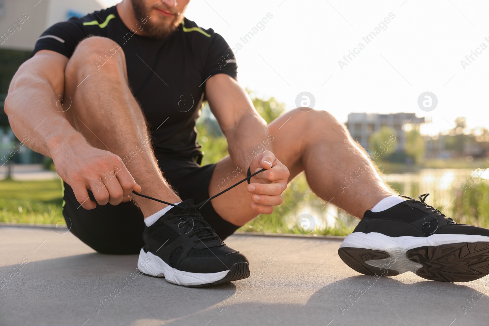 Photo of Man tying shoelaces before running outdoors on sunny day, closeup