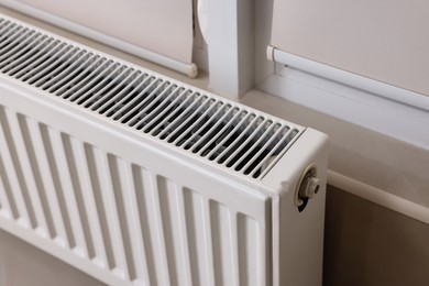 Photo of Modern radiator near window indoors, closeup. Central heating system