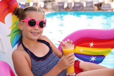 Photo of Happy girl with drink on inflatable unicorn in swimming pool