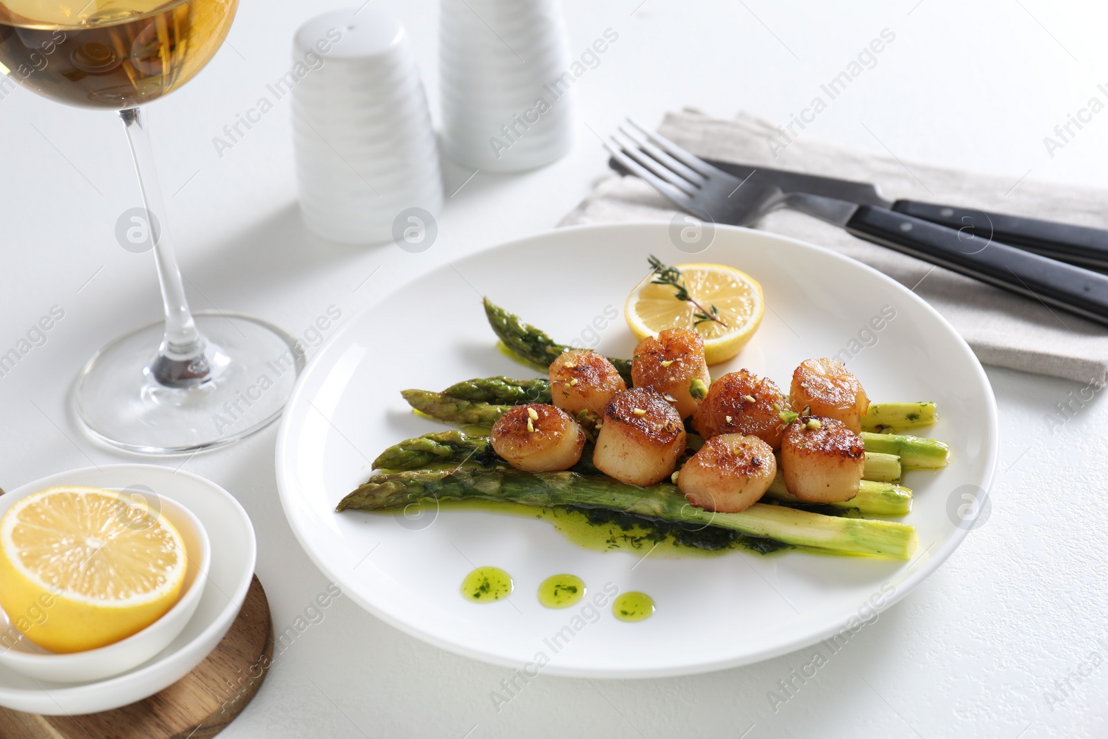 Photo of Delicious fried scallops with asparagus, lemon and thyme served on white table