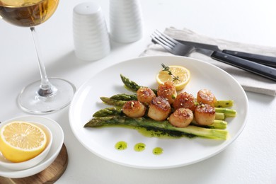 Delicious fried scallops with asparagus, lemon and thyme served on white table