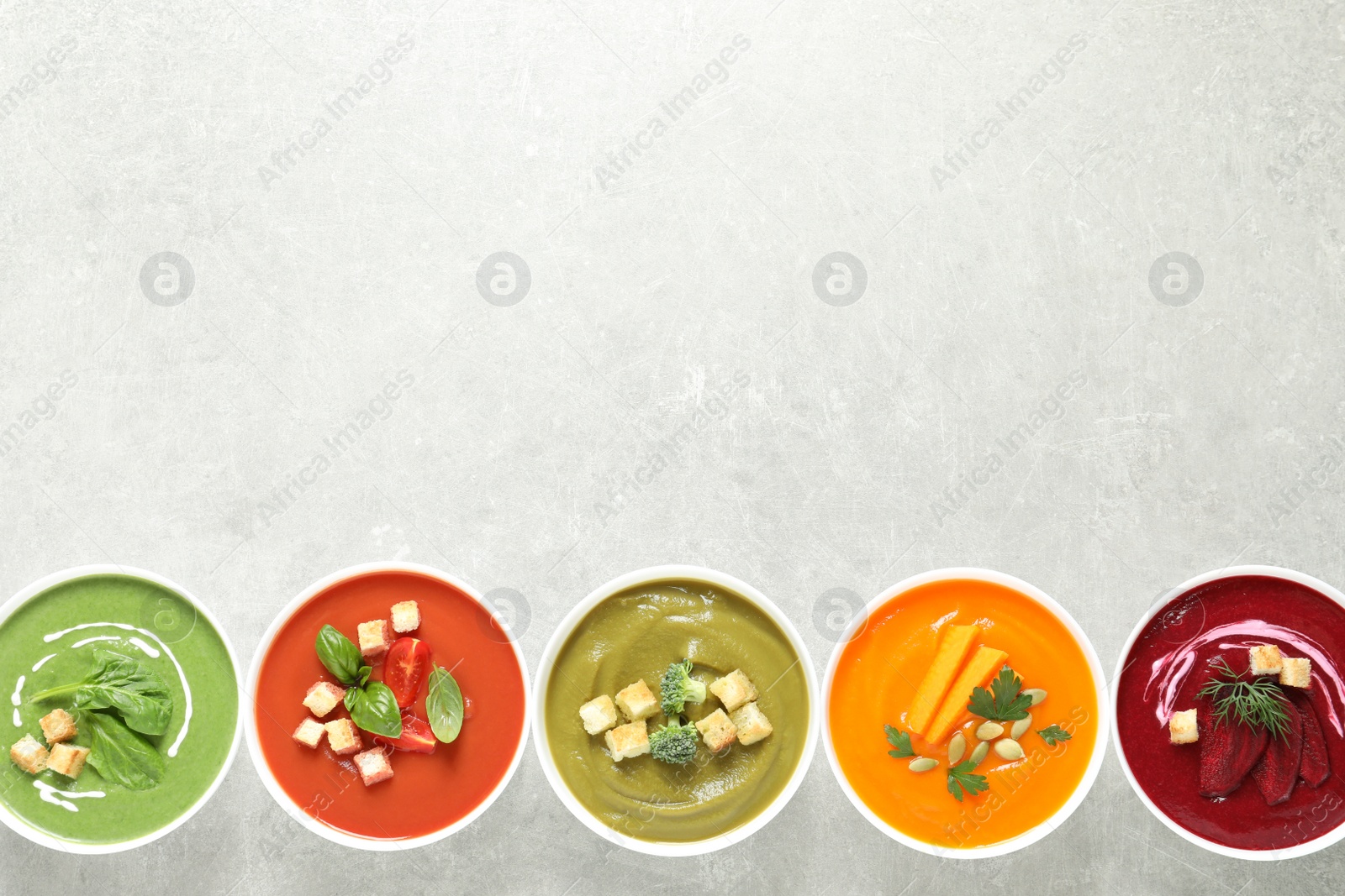 Photo of Various cream soups in bowls and space for text on grey background, top view