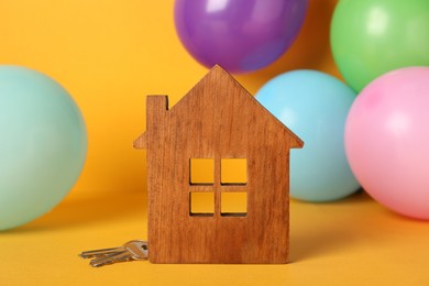 Photo of House model with keys and blurred balloons on yellow background. Housewarming party