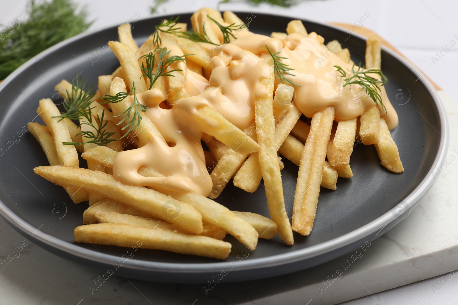 Photo of Delicious french fries with cheese sauce and dill on white table, closeup