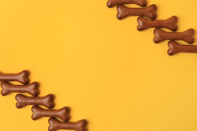 Bone shaped dog cookies on orange background, flat lay. Space for text