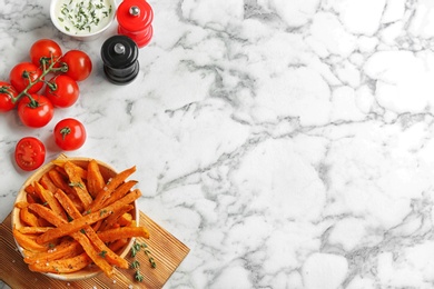 Flat lay composition with bowl of sweet potato fries on marble background. Space for text