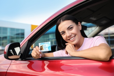 Photo of Happy young woman holding license while sitting in car. Driving school