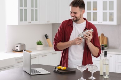 Photo of Man learning to make cocktail with online video on laptop at table in kitchen. Time for hobby