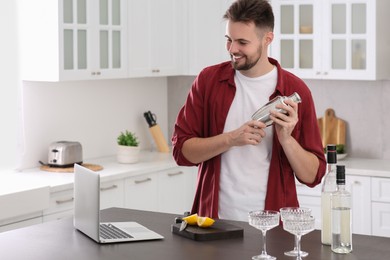 Man learning to make cocktail with online video on laptop at table in kitchen. Time for hobby