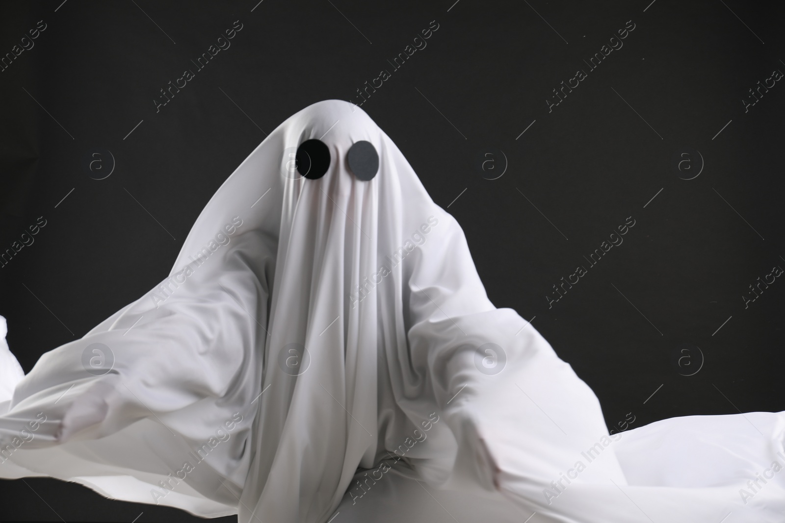 Photo of Creepy ghost. Person covered with white sheet on black background