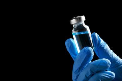 Photo of Doctor holding vial with medication on black background, closeup view and space for text. Vaccination and immunization